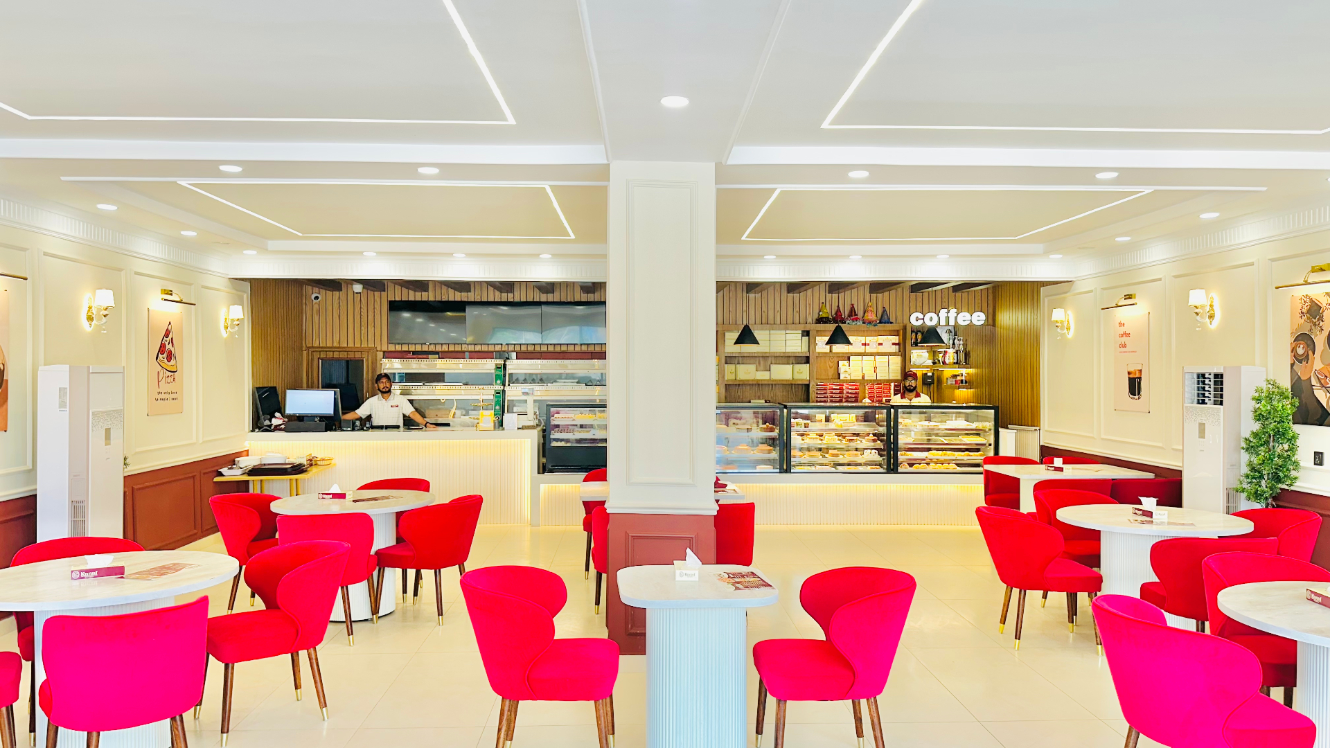 Bright, elegant café interior with round wooden tables, red upholstered chairs, and a cream-walled service counter